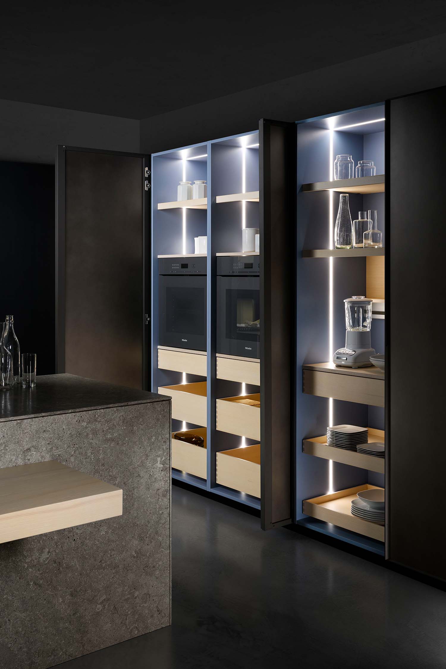 A detailed shot of an open kitchen drawer. The drawer's interior is a light wood, and it contains a neat wooden divider with compartments for cutlery and small kitchen tools.